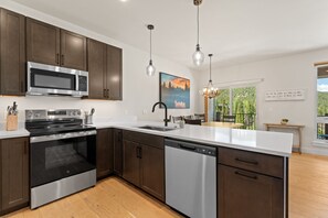 A modern kitchen with stainless steel appliances, dark wood cabinets, and a large island with a dishwasher. - Modern 3br Condo in Keystone (Keystone)