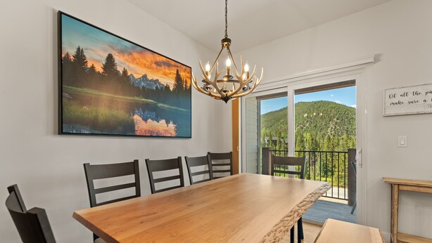 A dining area with a large wooden table, black chairs, a chandelier, and a painting of a mountain landscape. - Modern 3br Condo in Keystone (Keystone)