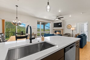 A modern kitchen with a large island, a dining area with a view, and a living room with a fireplace. - Modern 3br Condo in Keystone (Keystone)