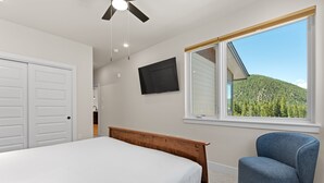 A bedroom with a bed, a chair, a TV, and a window with a view of a forested hill. - Modern 3br Condo in Keystone (Keystone)