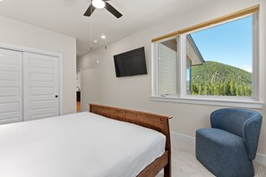 A bedroom with a bed, a chair, a TV, and a window with a view of a forested hill. - Modern 3br Condo in Keystone (Keystone)