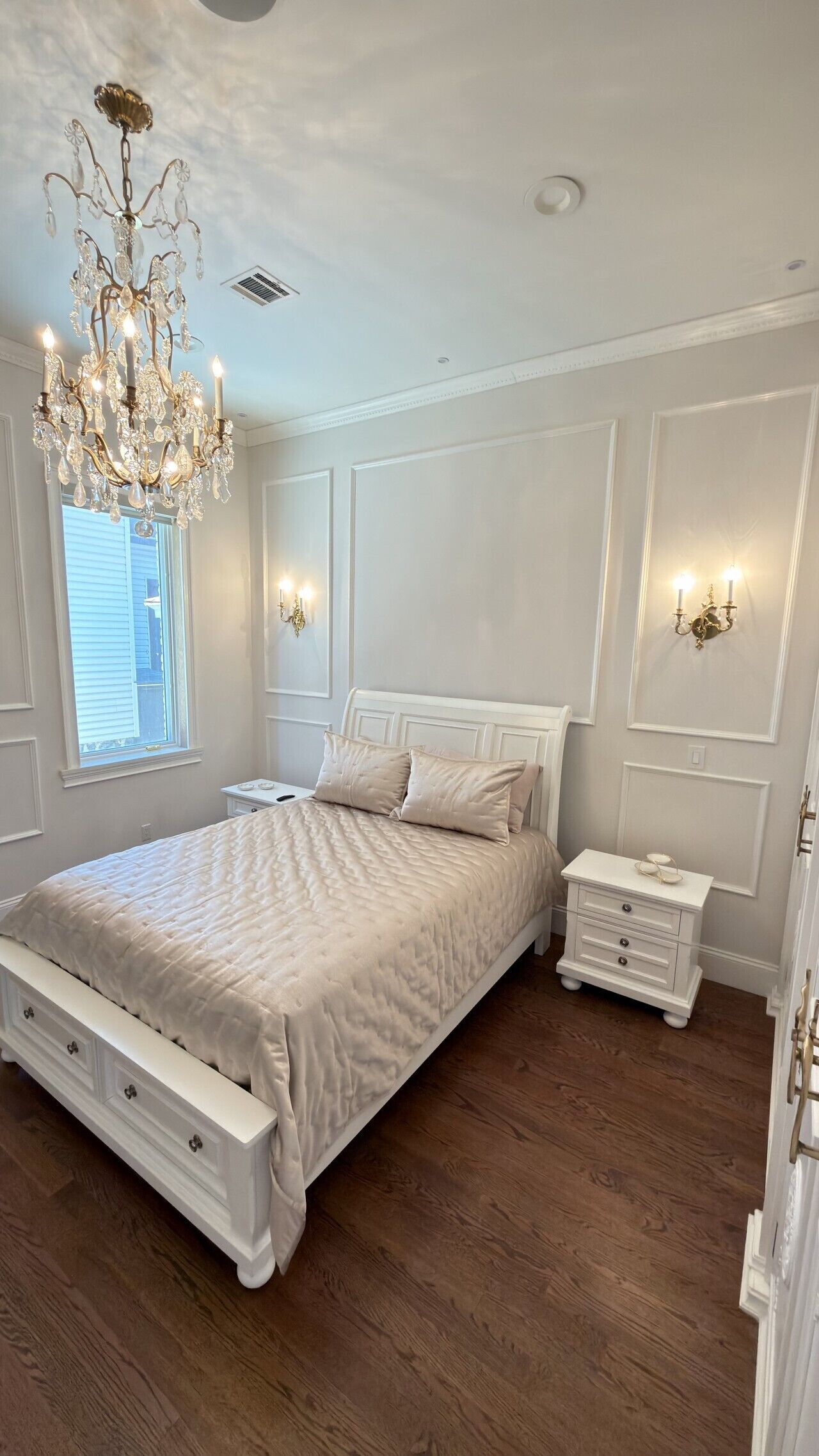 A bedroom with a large bed, a chandelier, bedside lamps, and a nightstand.