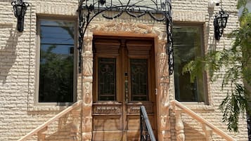 Un edificio con fachada de piedra, una entrada imponente con reja de hierro forjado y un conjunto de escalones de piedra que conducen a una puerta de madera.