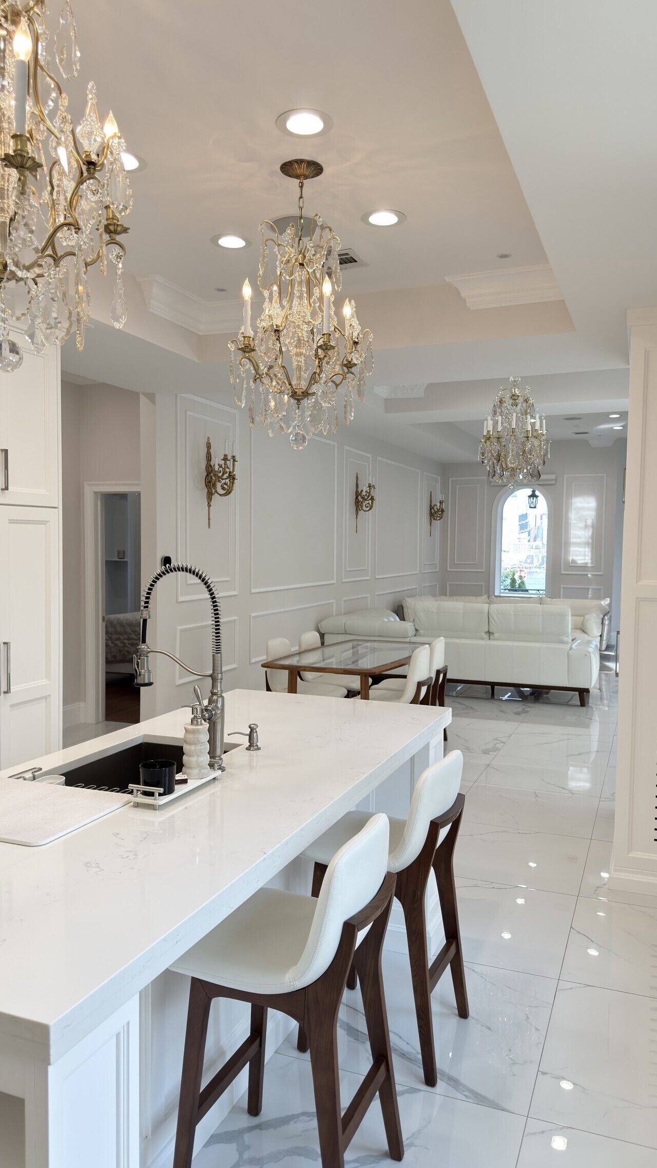 A modern kitchen with a central island, bar stools, a built-in sink, and a chandelier.