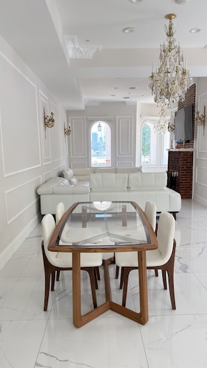A spacious living room with a central glass-top table surrounded by chairs, a white sofa, and a chandelier. - Elegant 2-Bedroom Apartment with Stunning Manhattan Views and Free Parking (Weehawken Township)