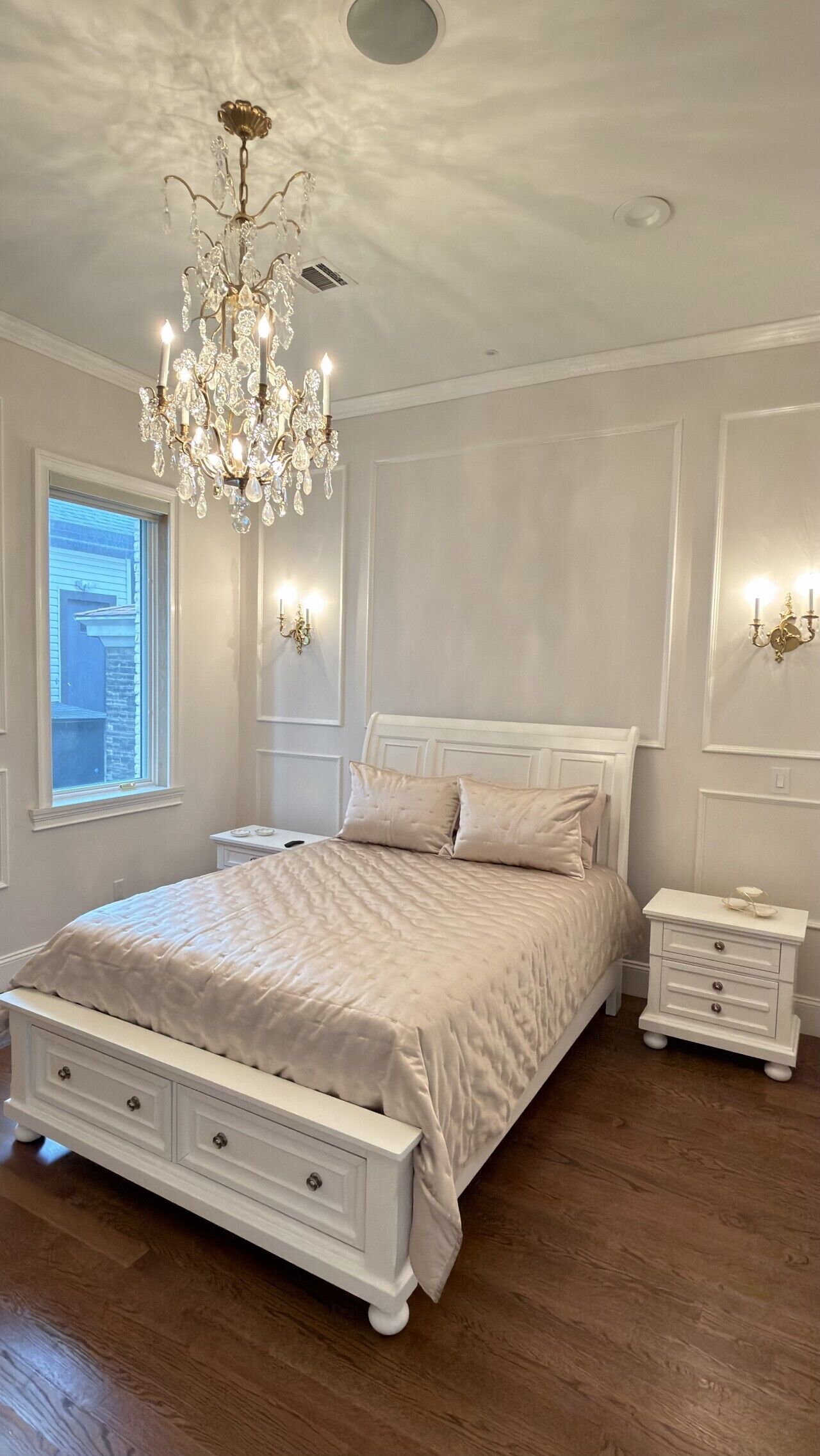 Une chambre à coucher avec un grand lit, un lustre, une table de chevet et une fenêtre.