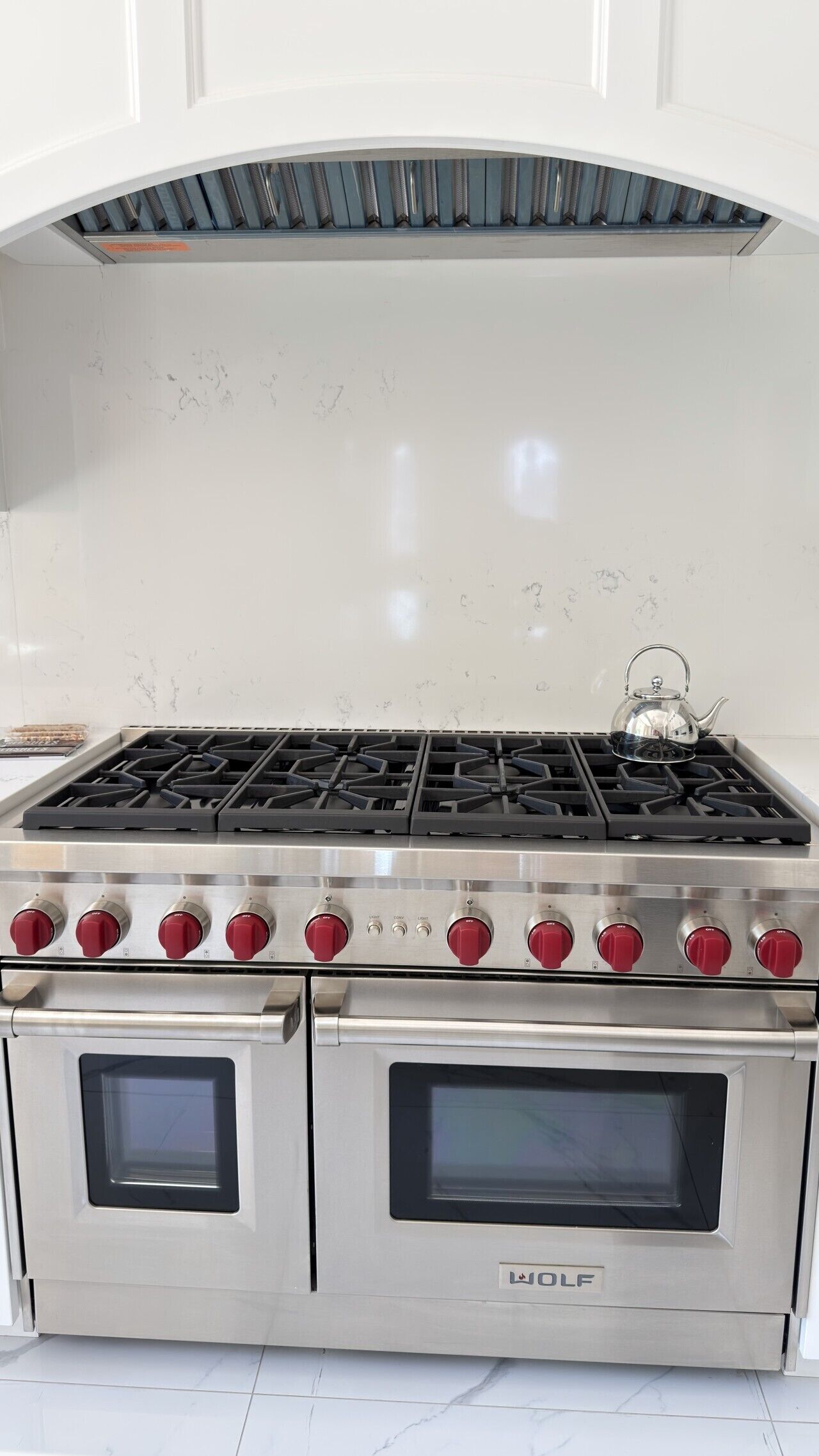 A stainless steel Wolf oven with a stovetop and two ovens, set against a white tiled backsplash.