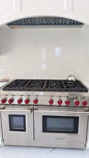 A stainless steel Wolf oven with a stovetop and two ovens, set against a white tiled backsplash. - Elegant 2-Bedroom Apartment with Stunning Manhattan Views and Free Parking (Weehawken Township)