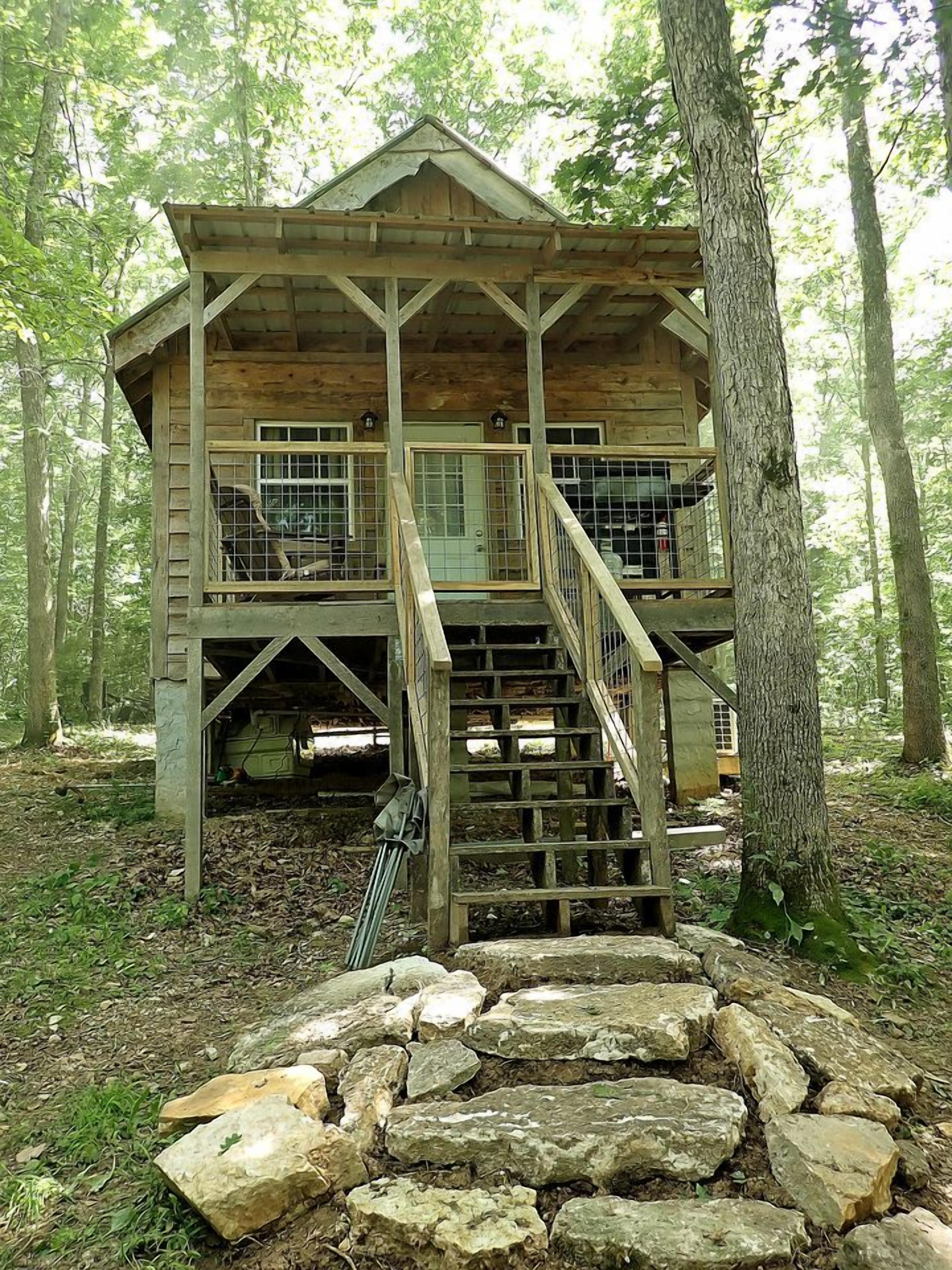 A wooden cabin with a staircase leading to a deck, surrounded by trees.