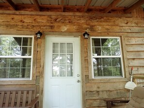 A wooden cabin with a white door, two windows, and a bench outside. - Tiny Cabin with Fire Pit & Covered Porch Retreat in Salem, Missouri (Salem)