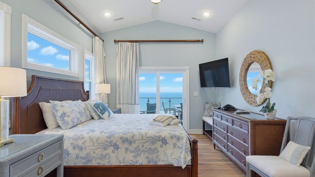 Een slaapkamer met een bed, nachtkastjes, een kaptafel, een televisie en uitzicht op zee.