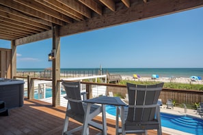 Eine Holzterrasse mit Pool, Stühlen und Blick auf den Strand.