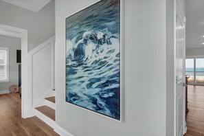 En trappa med trästeg och vita väggar, som leder upp till ett rum med en stor, abstrakt målning.