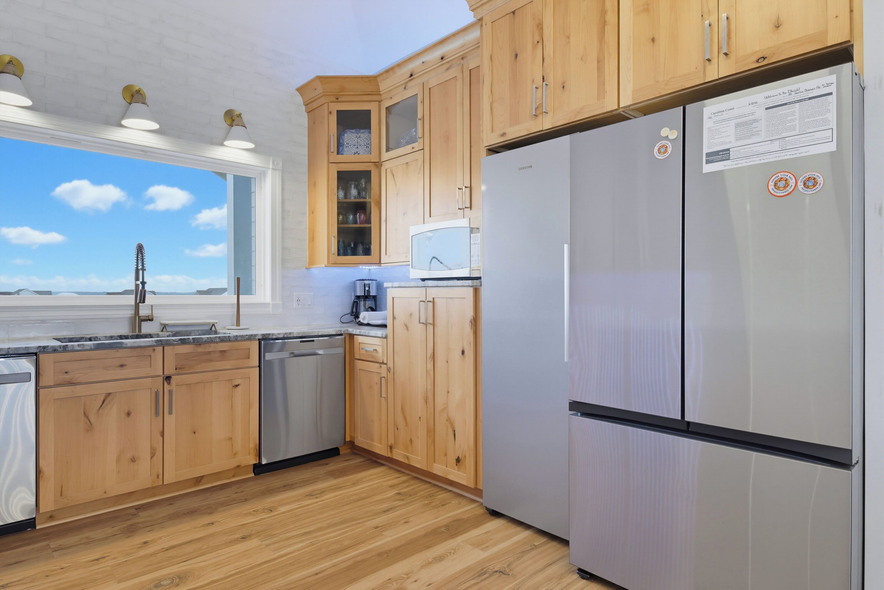 A modern kitchen with wooden cabinets, a stainless steel refrigerator, and a window with a view.