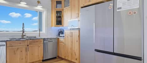 A modern kitchen with wooden cabinets, a stainless steel refrigerator, and a window with a view.