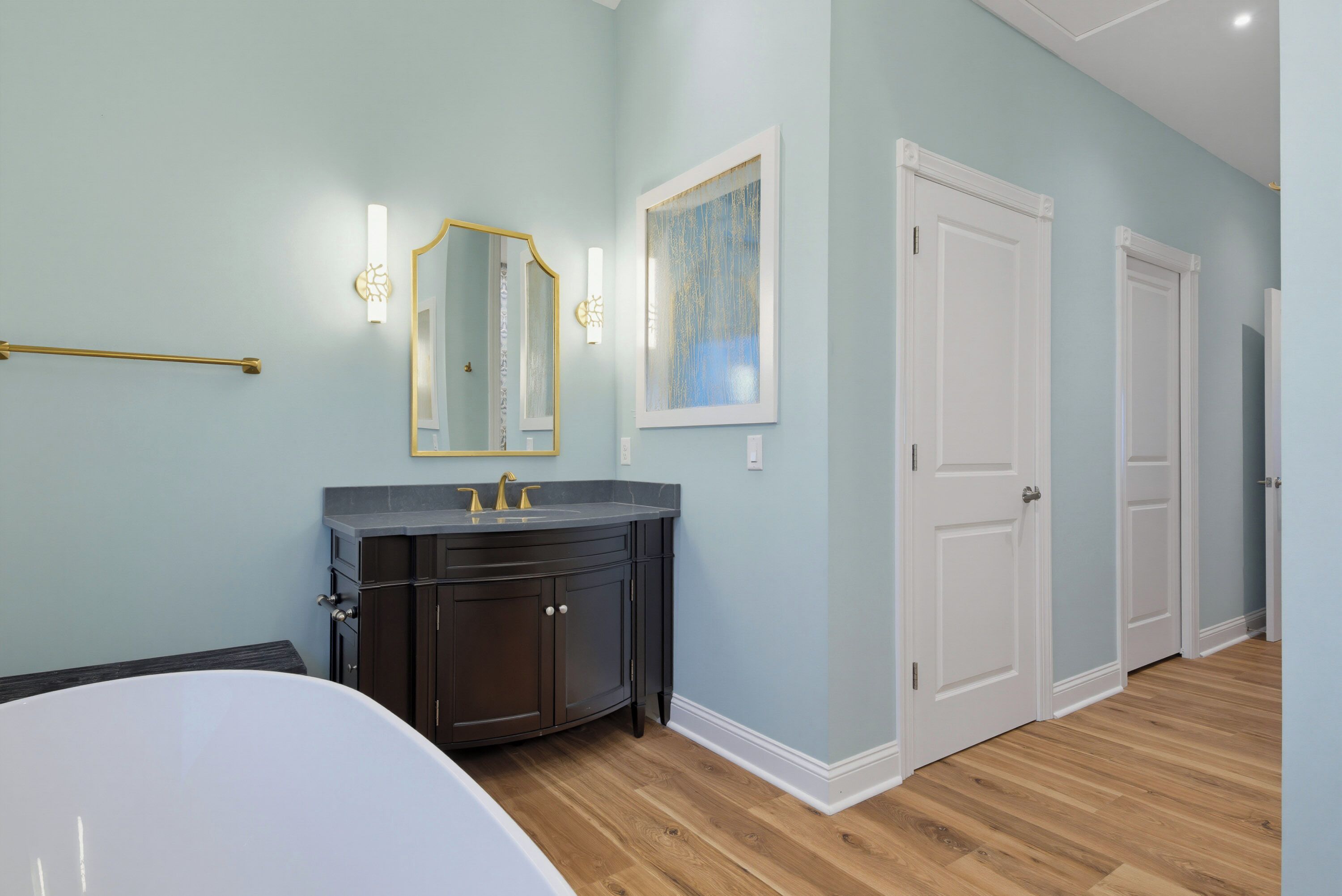 A bathroom with a bathtub, a vanity with a dark cabinet, and a mirror with wall sconces.