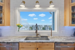 A kitchen with a large window, a stainless steel sink, wooden cabinets, and a marble countertop. - Oceanfront pool with theater and games (North Topsail Beach)