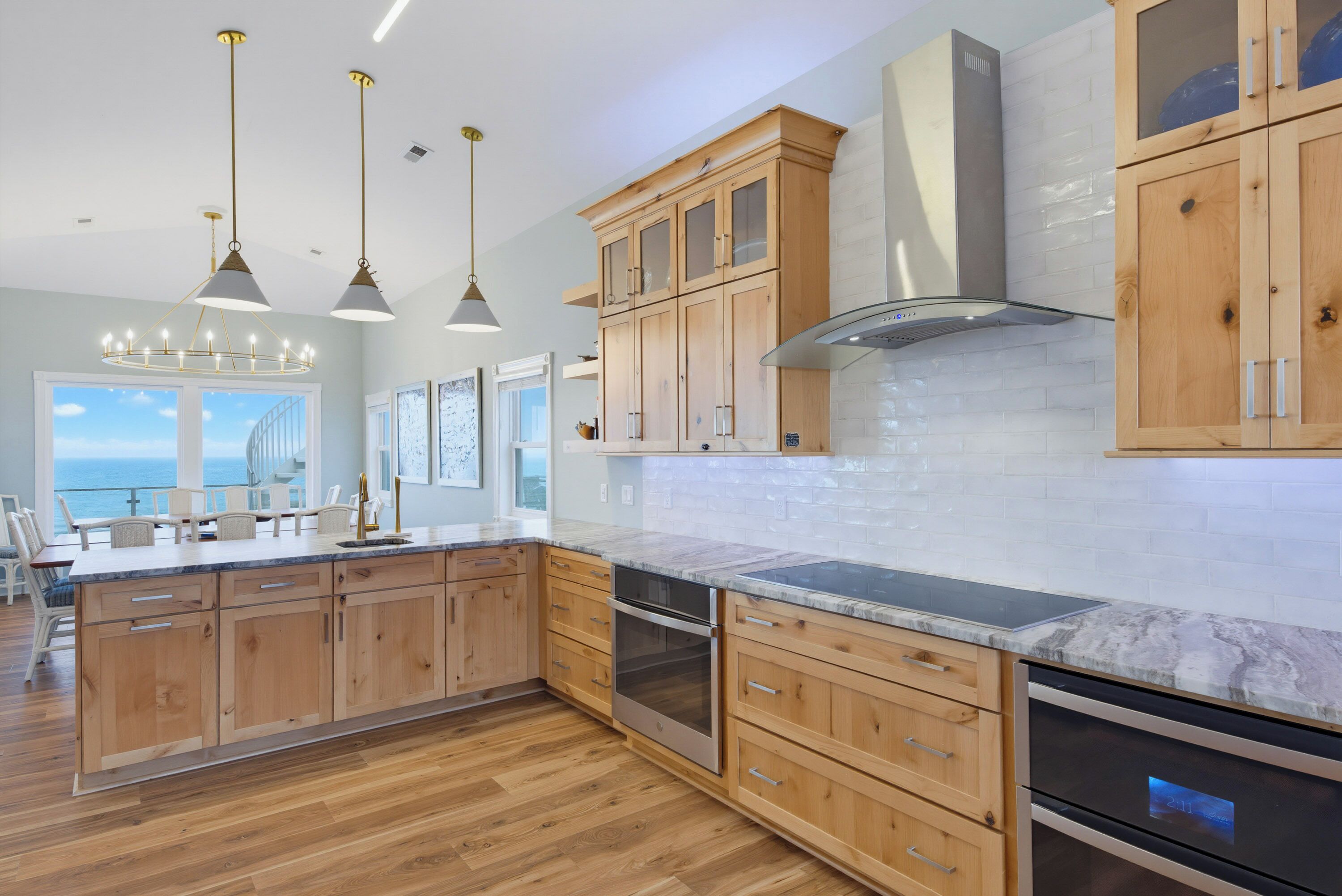A modern kitchen with wooden cabinets, a stainless steel range hood, and a large island with a built-in oven.