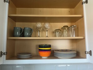 Un armario de cocina con estantes que contienen diversos utensilios de cocina, como tazas, copas de vino y platos.
