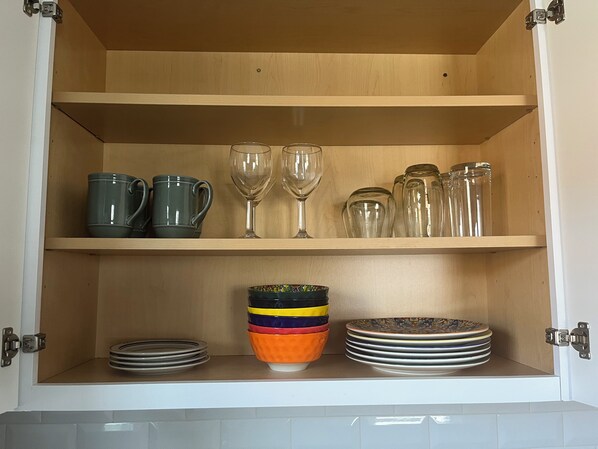 Eine Küchenschrank mit Regalen, auf denen verschiedene Küchenutensilien wie Tassen, Weingläser und Teller Platz finden.