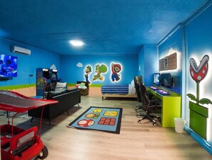 Una habitación con techo azul, una cama con manta azul y blanca a rayas, un escritorio con computadora y un carrito rojo.