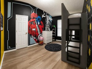 Ein Zimmer mit Etagenbett, weißem Schminktisch und Wandbild, sowie einem Fenster mit Jalousien.