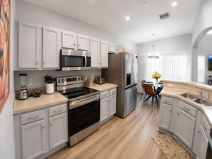 A modern kitchen with white cabinetry, stainless steel appliances, and a dining area with a table and chairs. - 5BR Fantastic Villa  Pool & Game Room Near Disney (Kissimmee)
