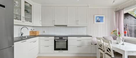 A modern kitchen with white cabinetry, a built-in oven, and a dining area with a table and chairs.