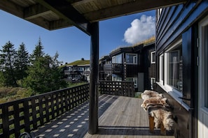 A wooden deck with a black fence, a dog, and a building with multiple windows and balconies. - Modern apartment in Hafjell (Gudbrandsdalen)