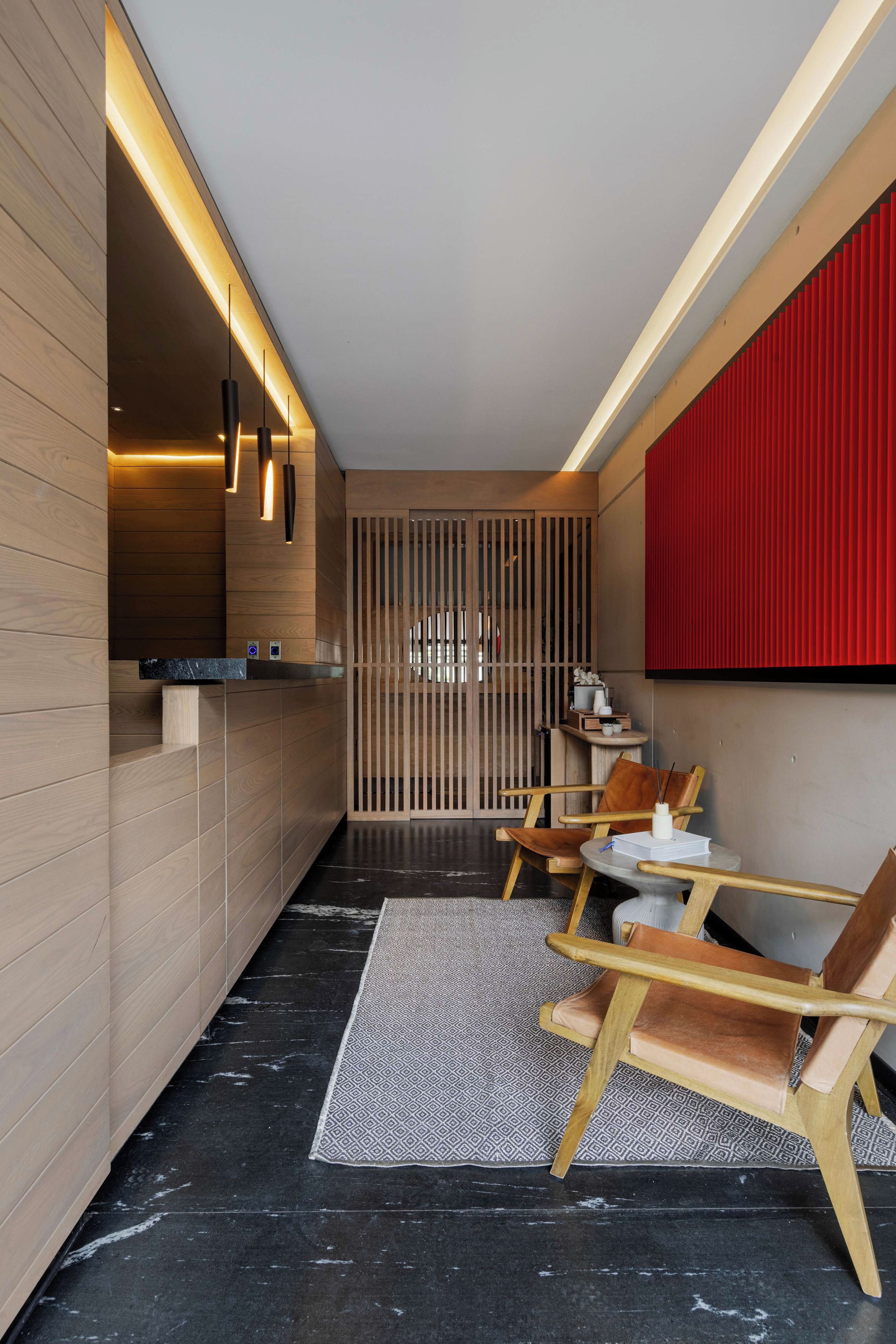 A modern interior with wooden panel walls, a black marble floor, and a seating area with wooden chairs and a small table.