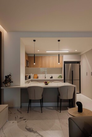 A modern kitchen with a central island, two chairs, a refrigerator, pendant lights, and a marble floor. - Family 2BR Apartment with Street-View Balcony in Polanco (Ciudad de México)