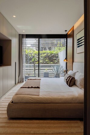 Un dormitorio moderno con una cama grande, un televisor de pantalla plana y vistas a la vegetación a través de una puerta corrediza de vidrio.