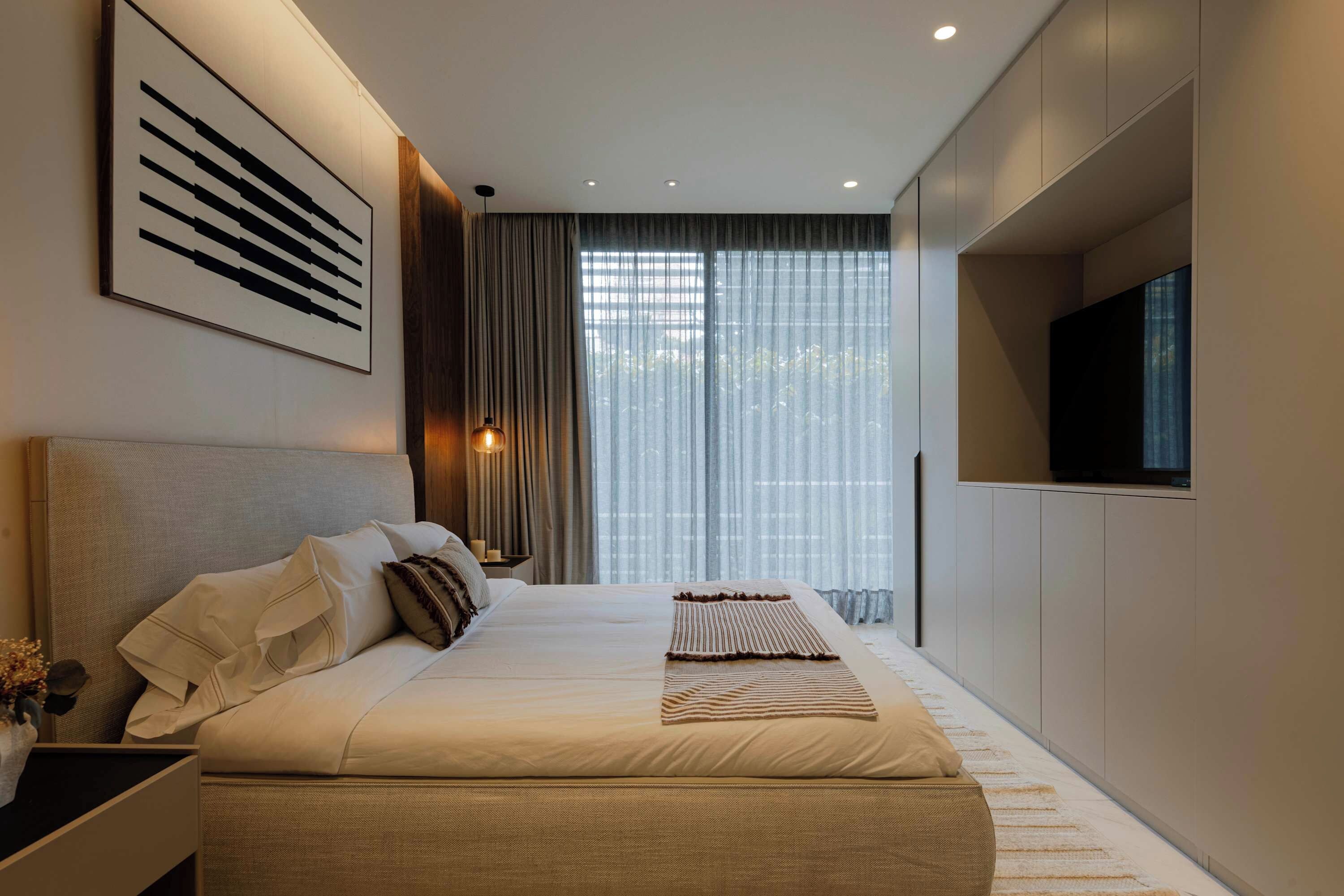 A modern bedroom with a large bed, a bedside table, a TV, and a window with curtains.