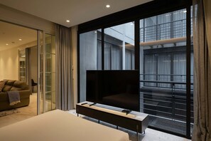 Quarto de hotel moderno com uma cama grande, televisão de tela plana, um sofá e uma porta de vidro deslizante que dá para uma varanda com vista para a cidade.