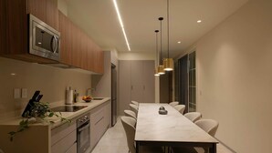A modern kitchen with a built-in microwave, a dining area with a long table and chairs, and pendant lighting. - Grand 3BR Apartment with Interior Balcony in Polanco (Ciudad de México)