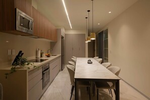 Uma cozinha moderna com micro-ondas embutido, uma área de refeições com uma mesa comprida e cadeiras, e iluminação pendente.