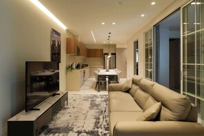 Ein modernes Wohnzimmer mit Flachbildfernseher, einem beigefarbenen Sofa und einem Essbereich mit Tisch und Stühlen.