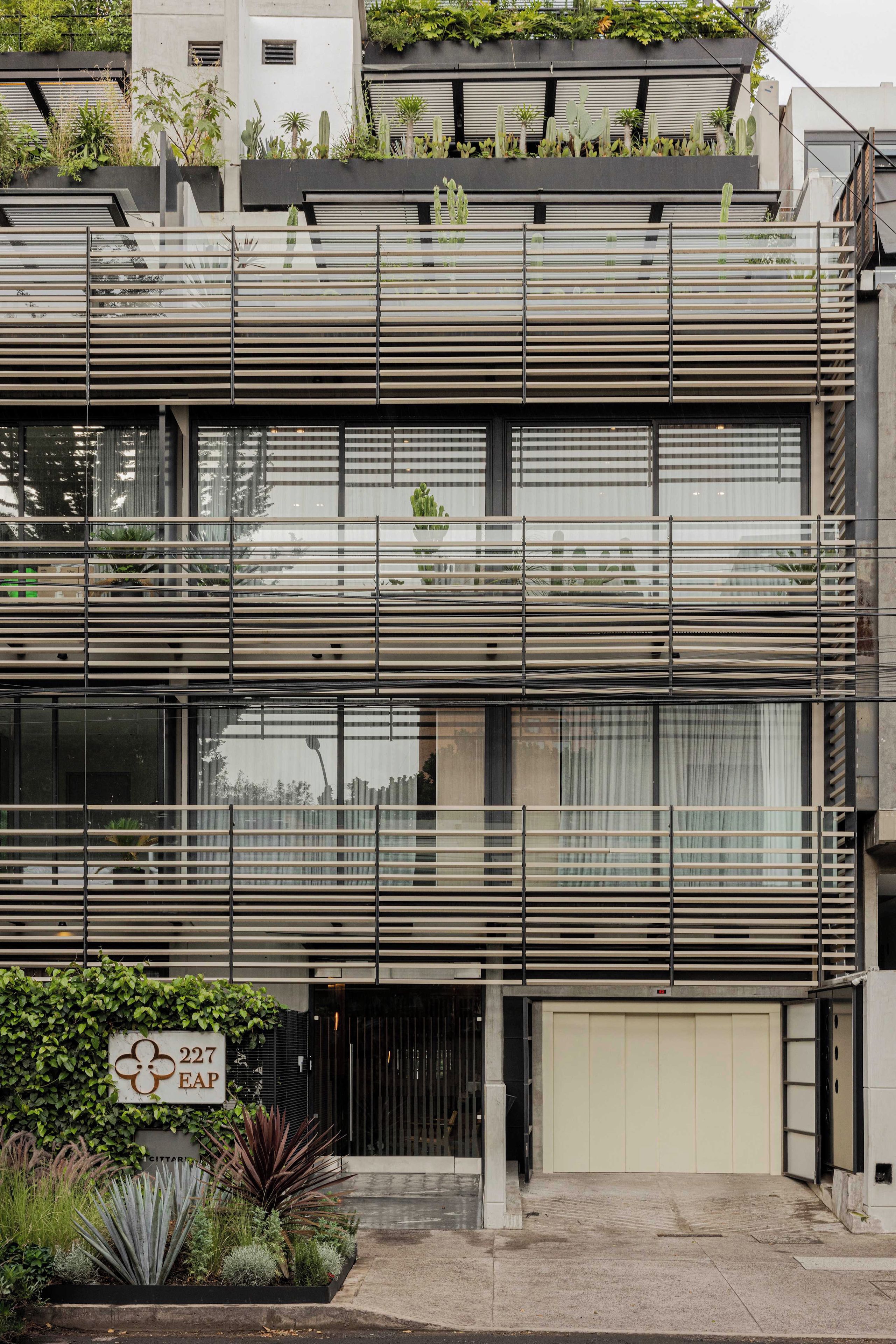 A multi-story building with horizontal slats on the facade, a gated entrance, and a sign with a flower and number.