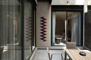 Ein moderner Außenbereich mit Holztisch und -stühlen, einer Glaswand und einem geometrischen Kunstwerk an der Wand.