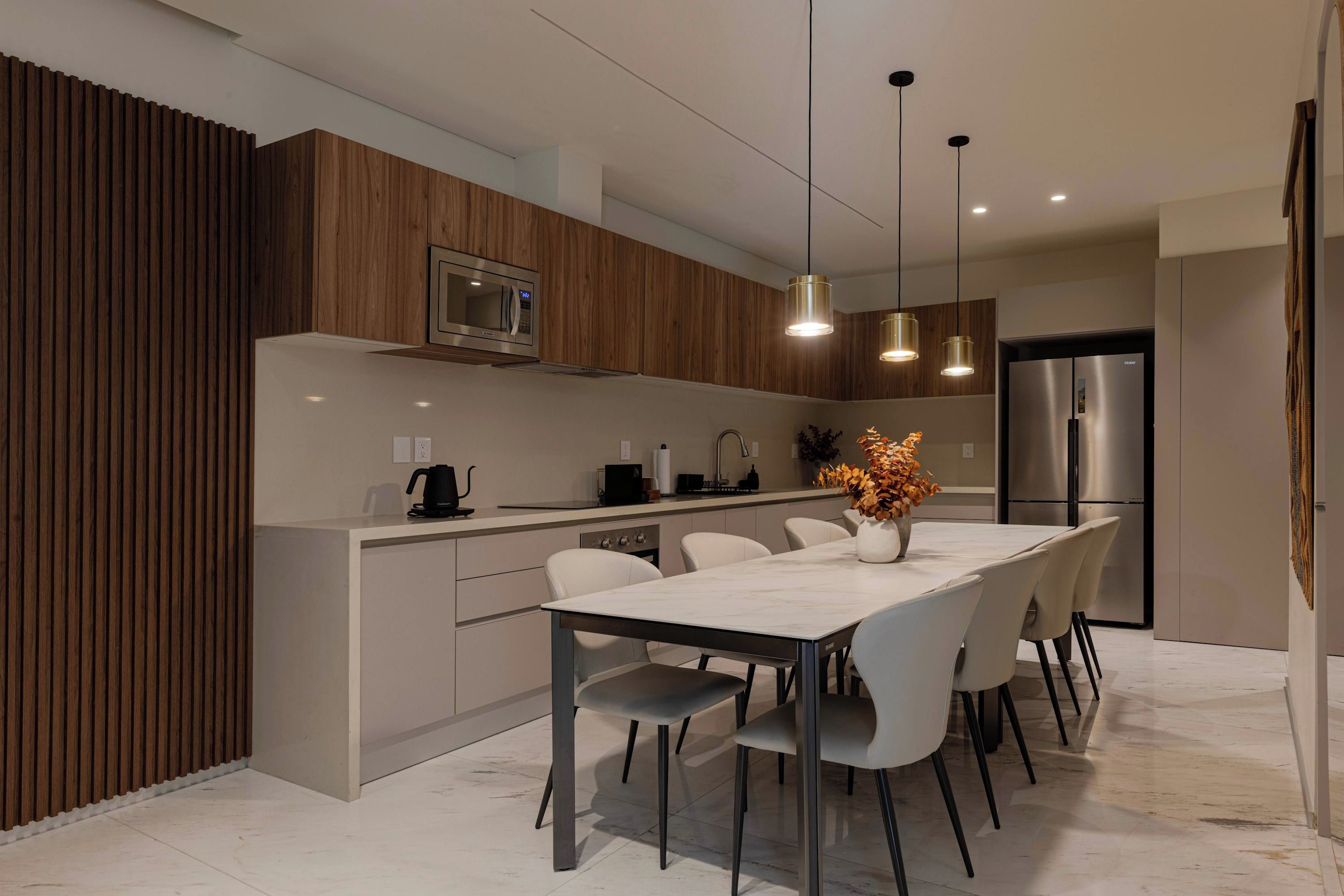 A modern kitchen with a built-in microwave, stainless steel refrigerator, and a dining area with a marble table and chairs.