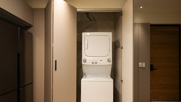 A compact laundry room with a front-loading washing machine and dryer, a wooden door, and a wall-mounted control panel. - Boutique Suite 2BR with AC and Balcony in Polanco (Ciudad de México)