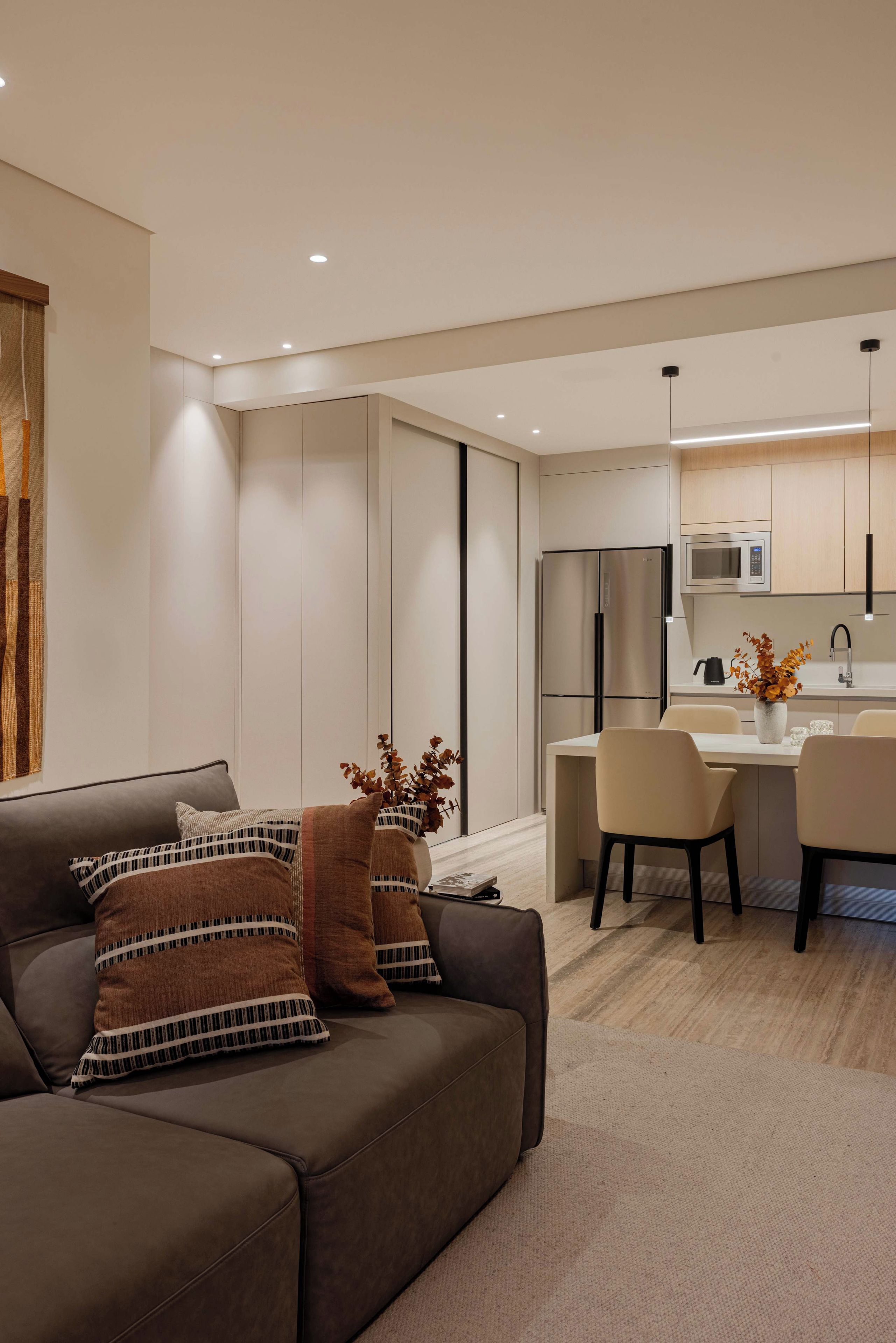 A modern living room with a sofa, a dining area with chairs, and a kitchen with a refrigerator and microwave.