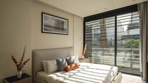 A modern bedroom with a large bed, a nightstand, a framed picture, and a view through a large window. - Boutique Suite 2BR with AC and Balcony in Polanco (Ciudad de México)