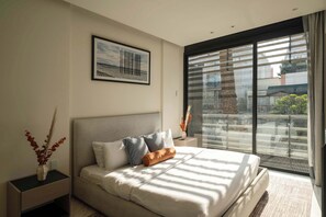 Ein modernes Schlafzimmer mit einem großen Bett, einem Nachttisch, einem gerahmten Bild und Blick durch ein großes Fenster.