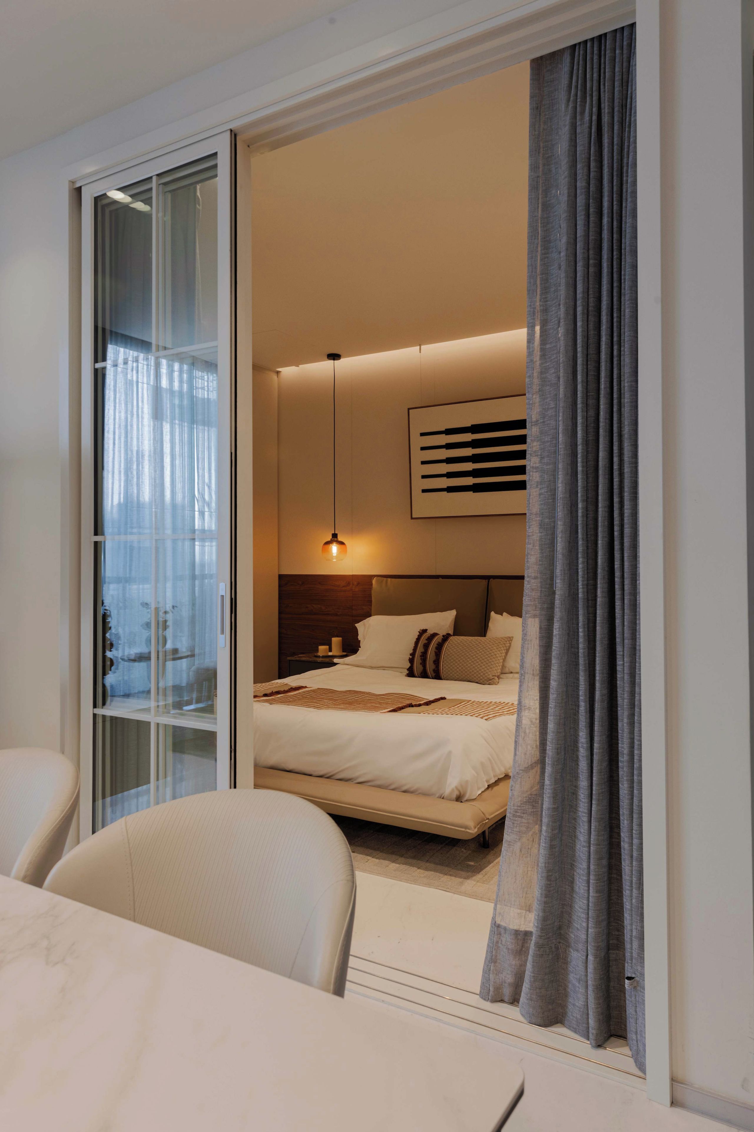 A modern hotel room with a bed, a bedside table, a lamp, and a view through a glass door.