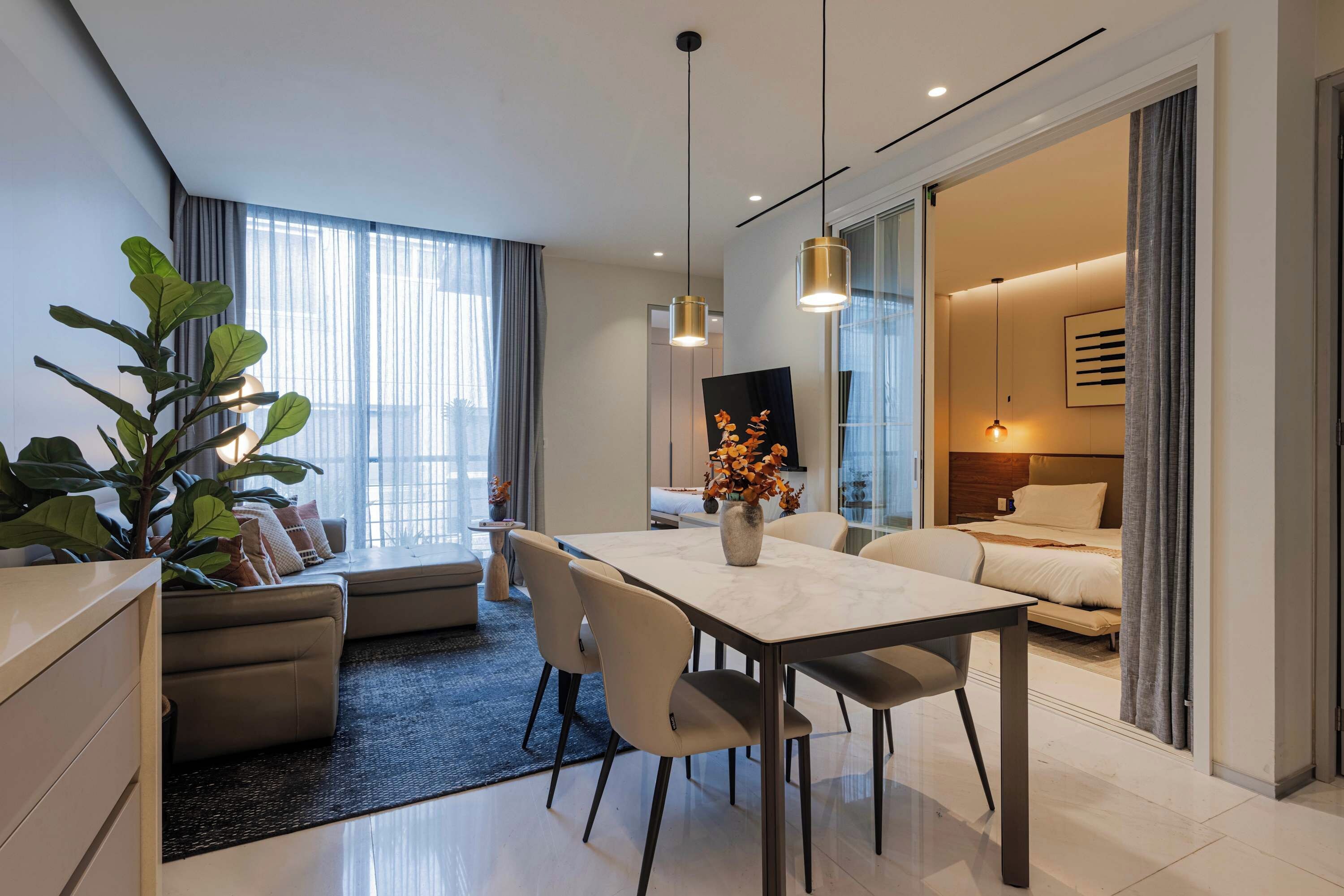 Moderni hotellihuone, jossa on ruokailutila, sohva, suuri huonekasvi ja näkymä kaupunkiin.