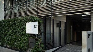 Ein moderner Gebäudeeingang mit Nummernschild, Metallgitter und einer Hecke.