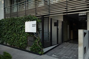 Ein moderner Gebäudeeingang mit Nummernschild, Metallgitter und einer Hecke.