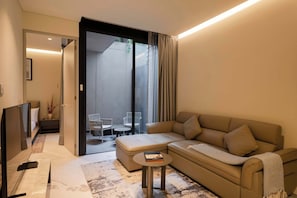 A modern living room with a sofa, a small round table, and a TV. There is a sliding glass door leading to an outdoor area with chairs. - Garden 1BR Apartment with Interior Terrace in Polanco (Ciudad de México)