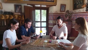 A group of people playing a card game at a table with a patterned tablecloth. - Copper Canyon Riverside Lodge (Batopilas)